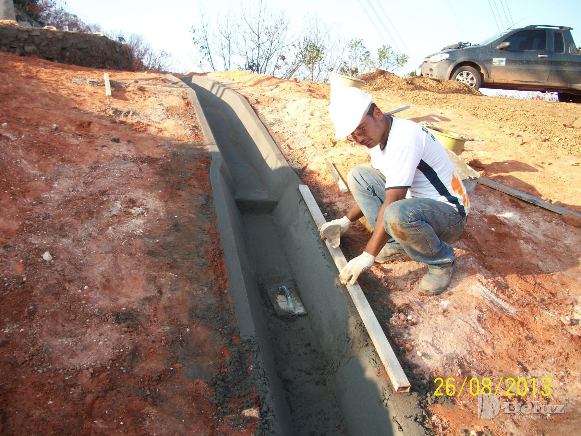 Colaborador instala canaleta de concreto na lateral do talude
