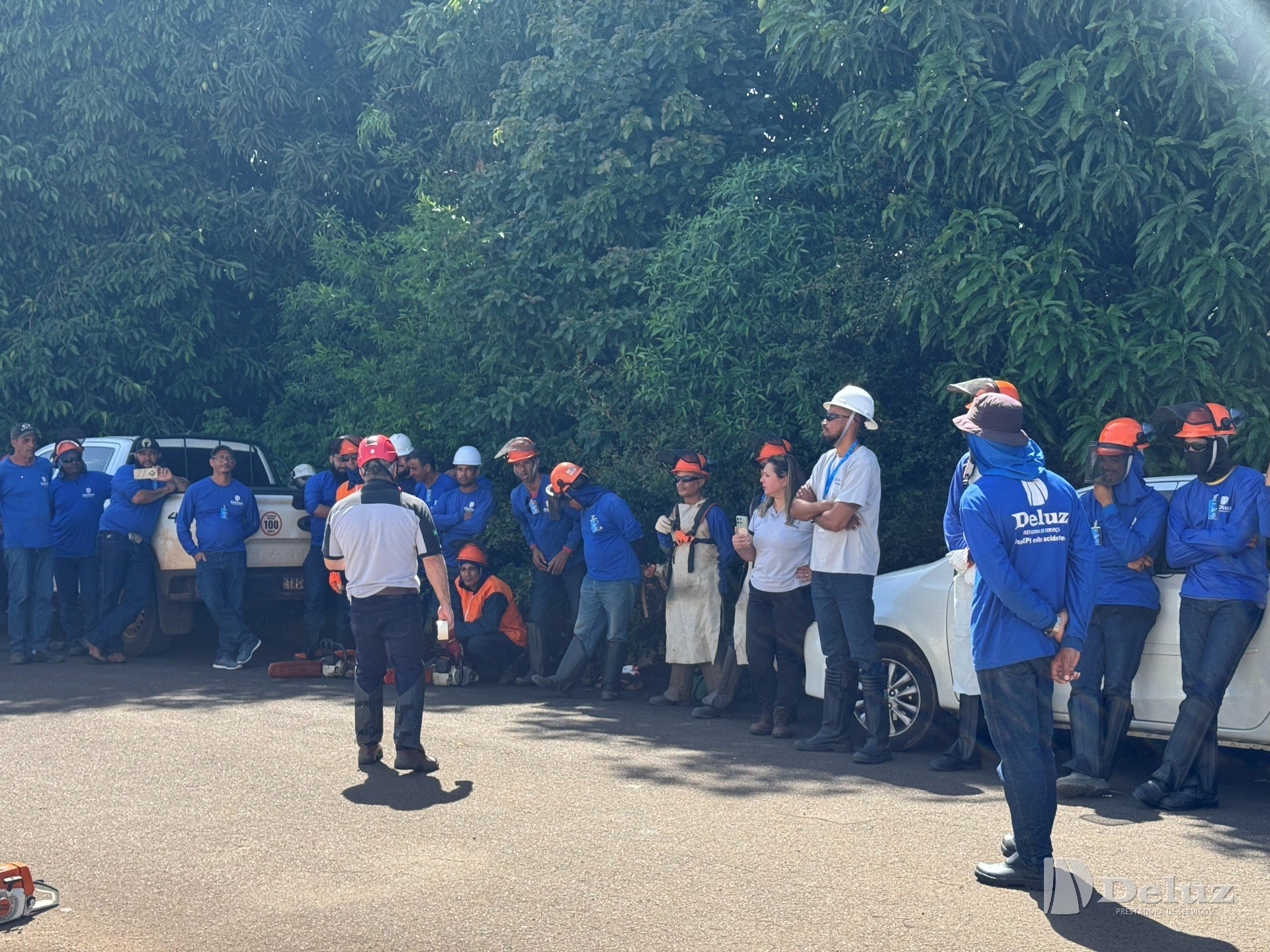 Instrutor orienta a turma reunida na área de prática, com capacetes, viseiras e protetores auriculares