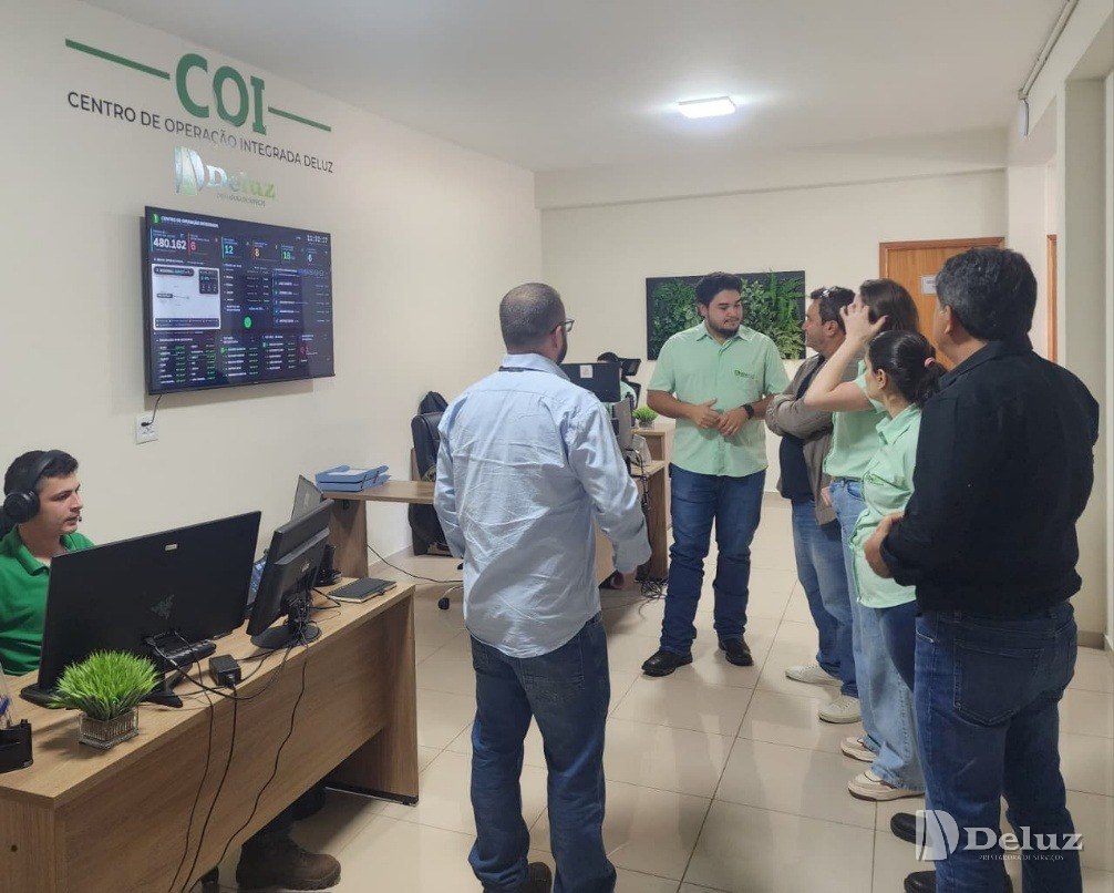 Equipe da Deluz apresenta o painel do Centro de Operação Integrada a um grupo de visitantes, com um operador acompanhando as telas