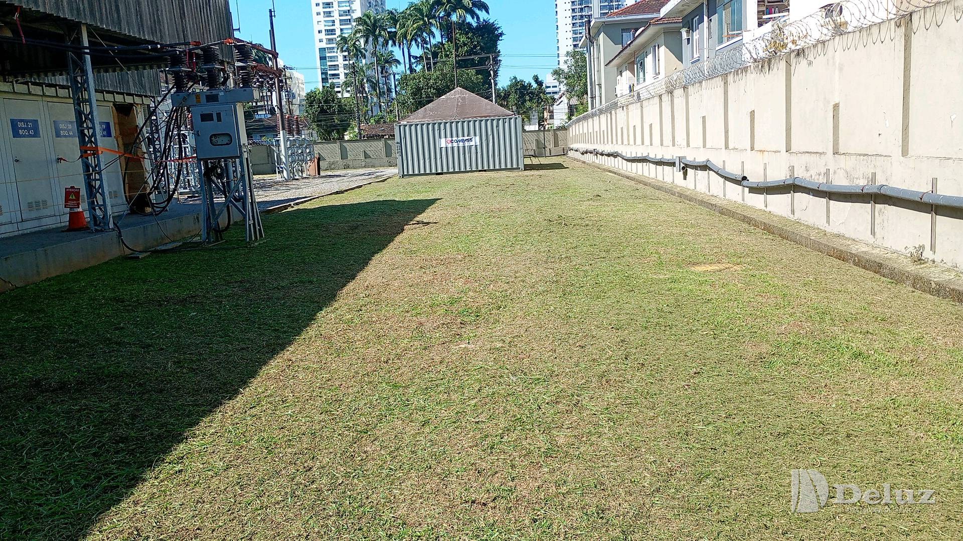 Pátio de subestação com a grama aparada e os equipamentos ao fundo